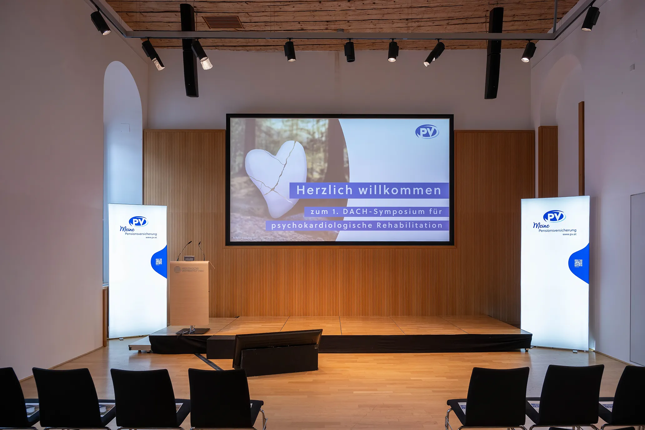 Leeres Podium mit Screen: Herzlich willkommen zum 1. DACH-Symposium für psychokardiologische Rehabilitation