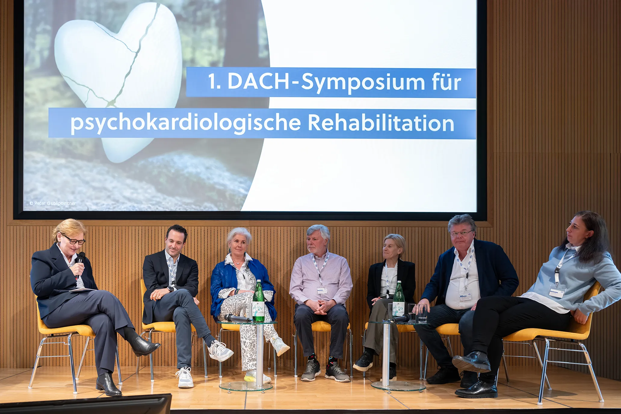 Podiumsdiskussion: 7 Diskutant*innen sitzen im Halbkreis auf dem Podium