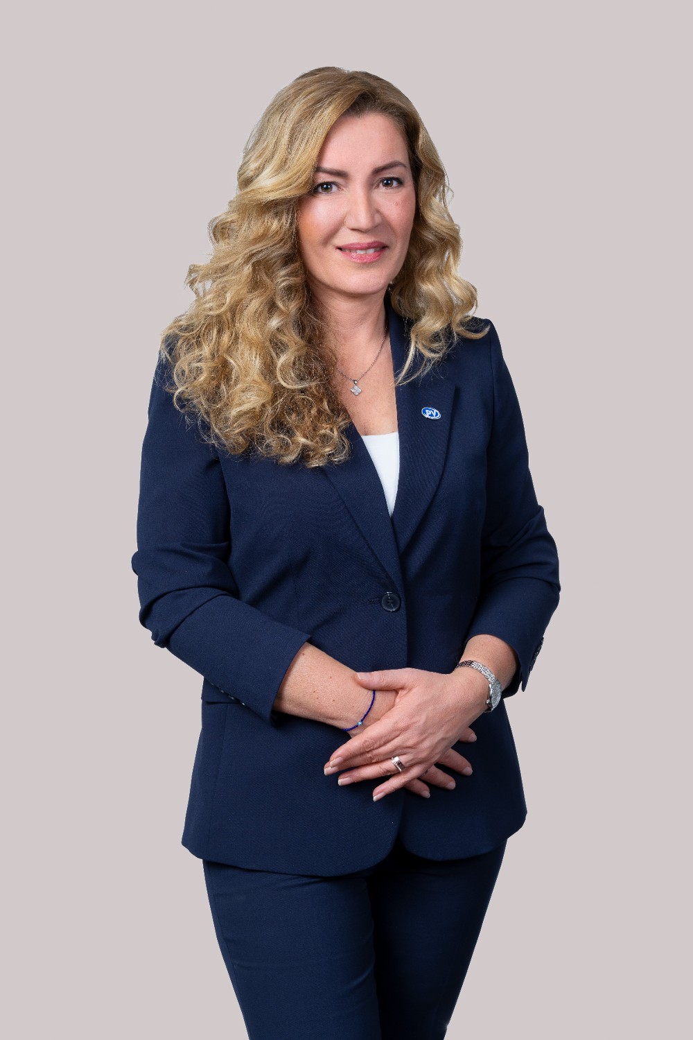Porträt von Mag.a Canan Aytekin, stellvertretende Generaldirektorin der Pensionsversicherung, mit lockigem blondem Haar und dunkelblauem Blazer