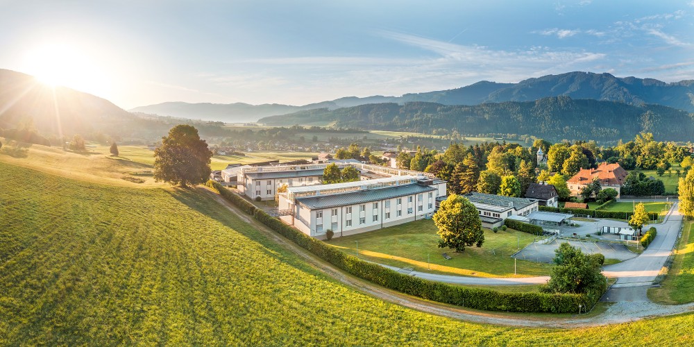 Blick auf das Reha-Zentrum Aflenz im warmen Licht mit Grünflächen und Hügeln im Hintergrund
