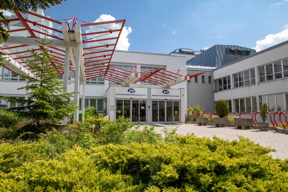 Eingangsbereich des Reha-Zentrums Hochegg mit weißer Fassade und roter Überdachung