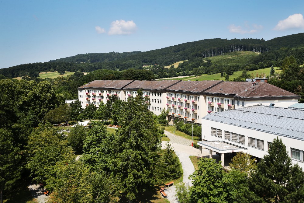Blick von oben auf das Reha-Zentrum Laab im Walde mit Bäumen, Grünflächen und Feldern im Hintergrund