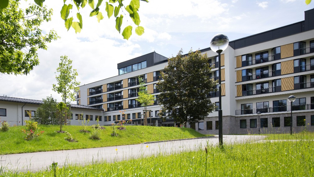 Außenansicht des Reha-Zentrums Saalfelden mit Bäumen und einer Grünfläche vor dem Gebäude