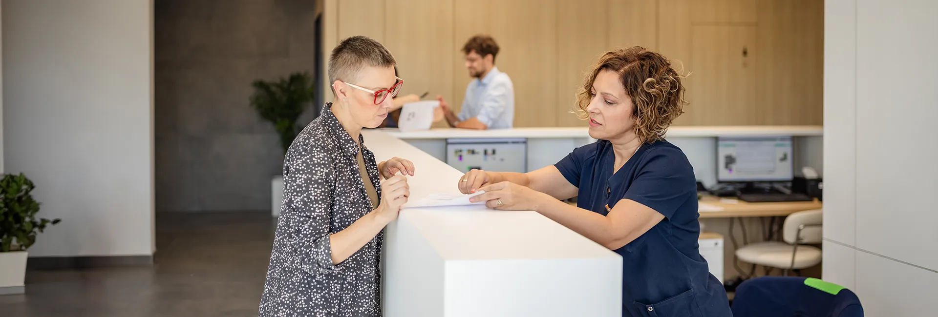 Mitarbeiterin bei der Anmeldung erkl&auml;rt betroffener Person den Ablauf der medizinischen Begutachtung